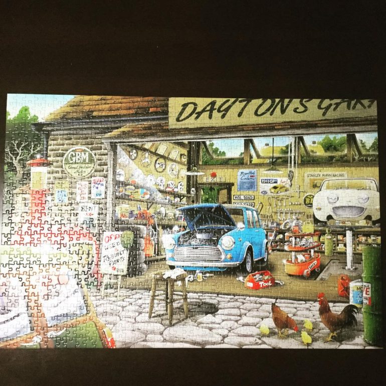 Picture of a completed jigsaw puzzle, "Dayton's Repair Garage", that shows an old-style garage with a blue car in the process of repair, lots of tools, and general clutter.