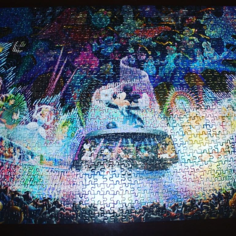 Picture of a completed jigsaw puzzle that shows Mickey Mouse directing a cascade of colored water and fireworks as an audience watches and various Disney couples dance.